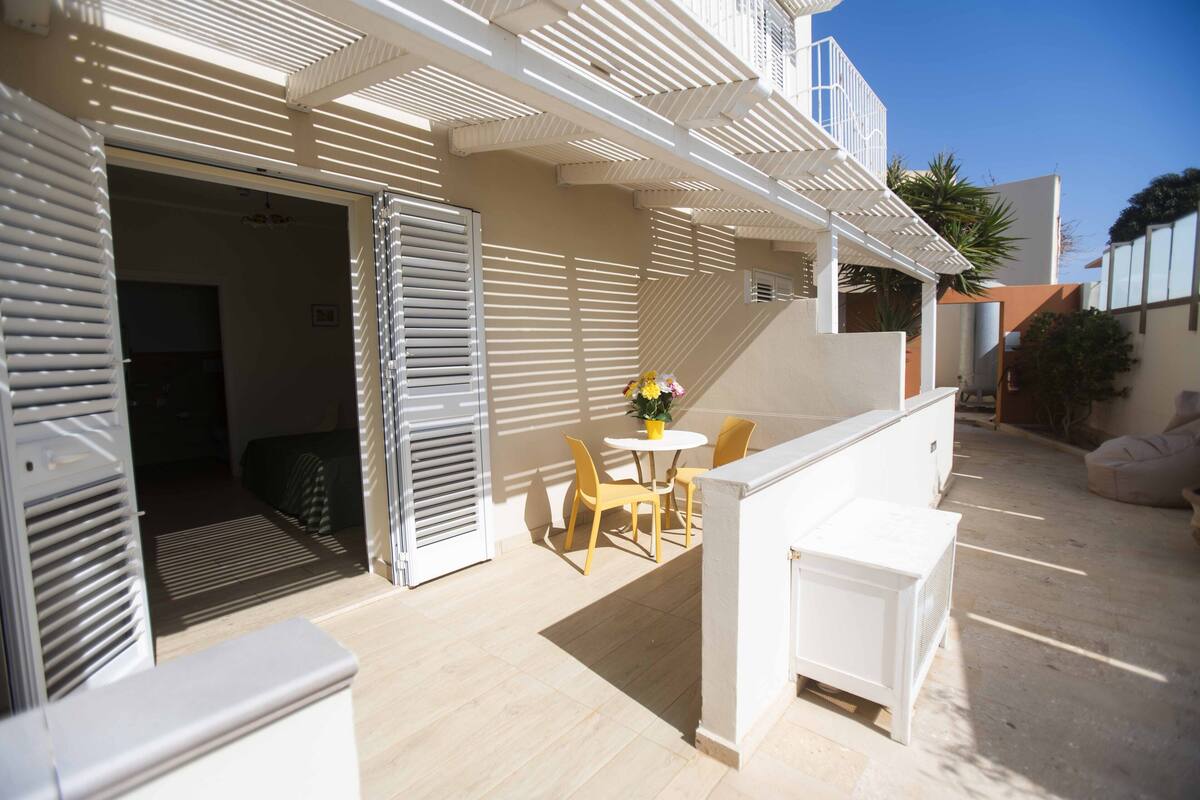 An outdoor patio with a table and chairs, a white air conditioning unit, and a door leading to an interior space.