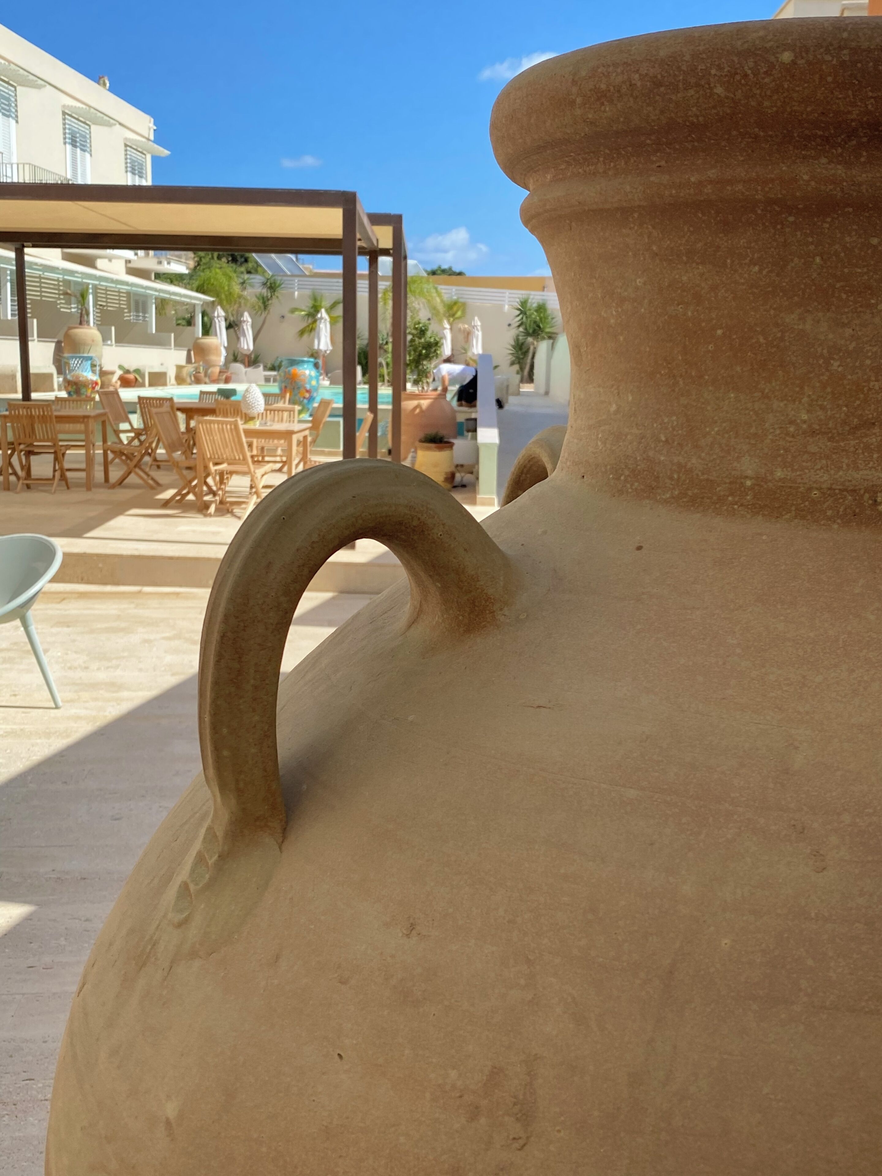 Un grand pot en céramique doté d’une anse, une piscine, du mobilier d’extérieur et un bâtiment en arrière-plan.