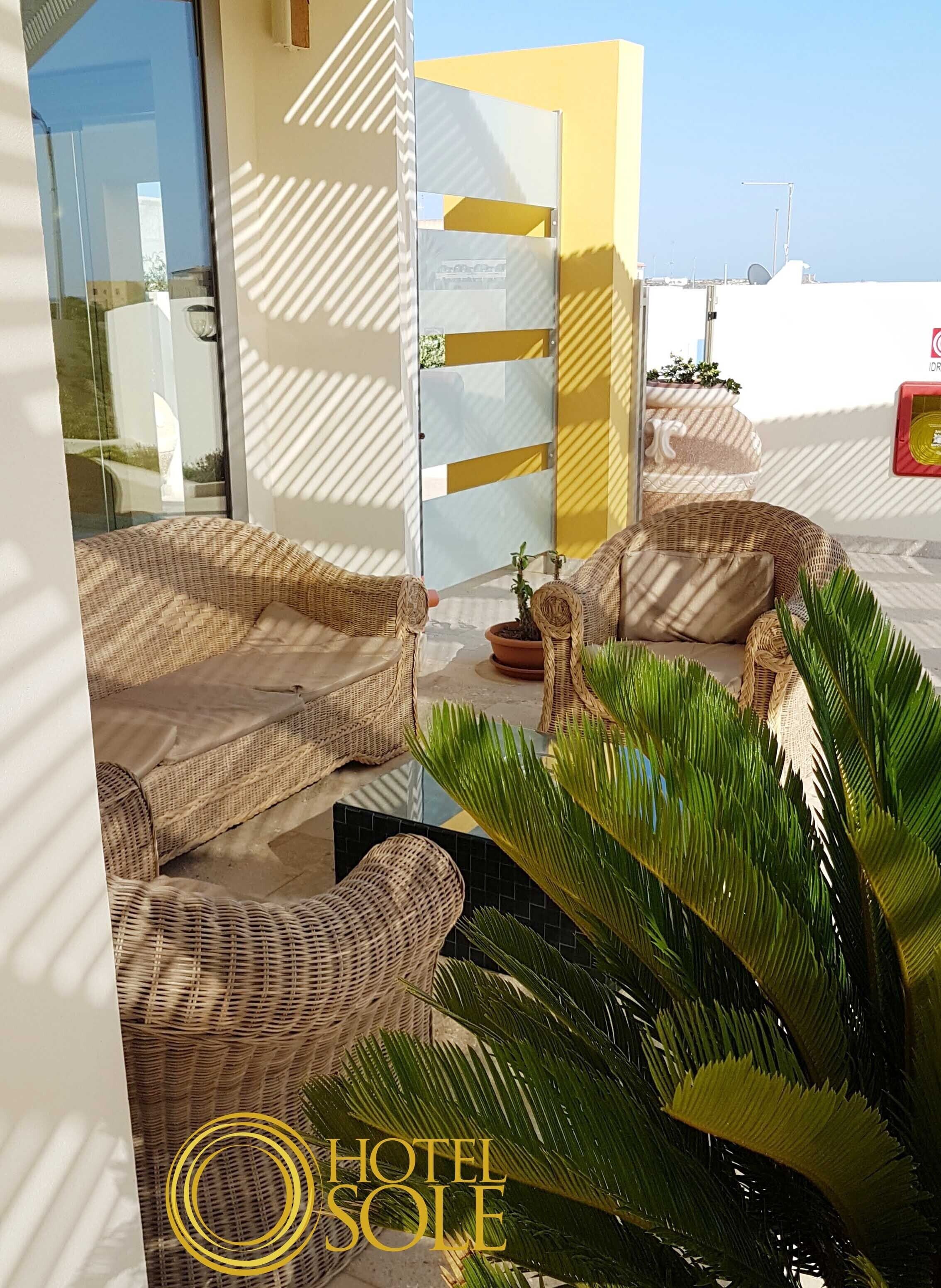 Une chambre d’hôtel meublée avec des meubles en osier, dotée d’une porte en verre et offrant une vue sur la mer.