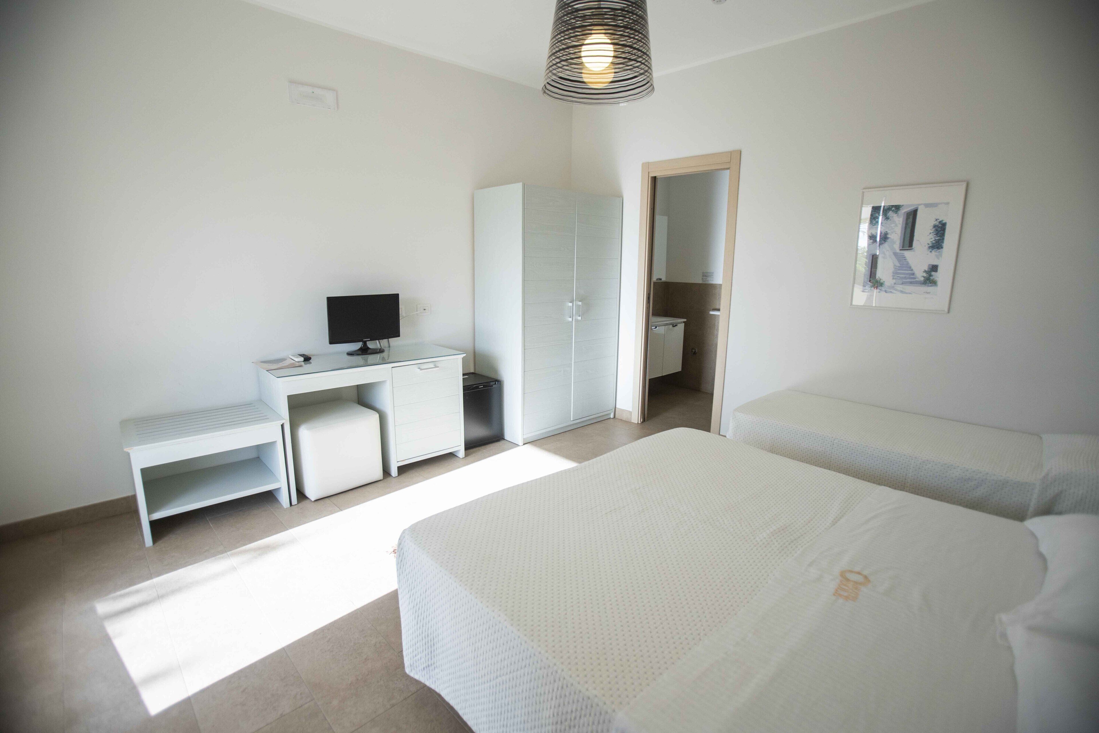 A bedroom with a desk, a bed, a wardrobe, and a shower.