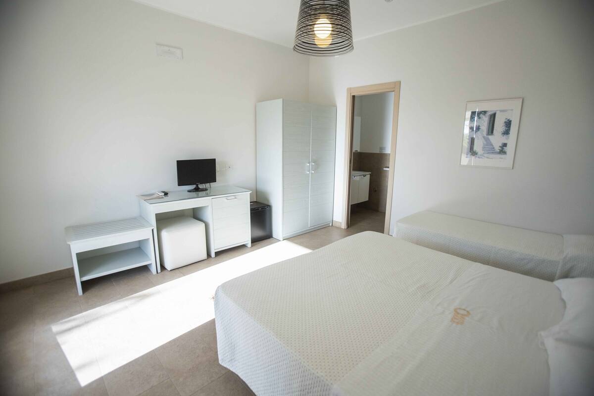 A bedroom with a desk, a bed, a wardrobe, and a shower.