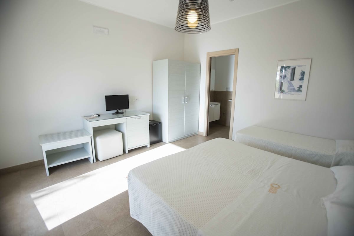 A bedroom with a desk, a bed, a wardrobe, and a shower.