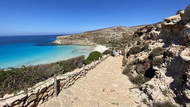A stone pathway leading to a coastal area with clear blue waters and rocky terrain. - Hotel Sole (Lampedusa)