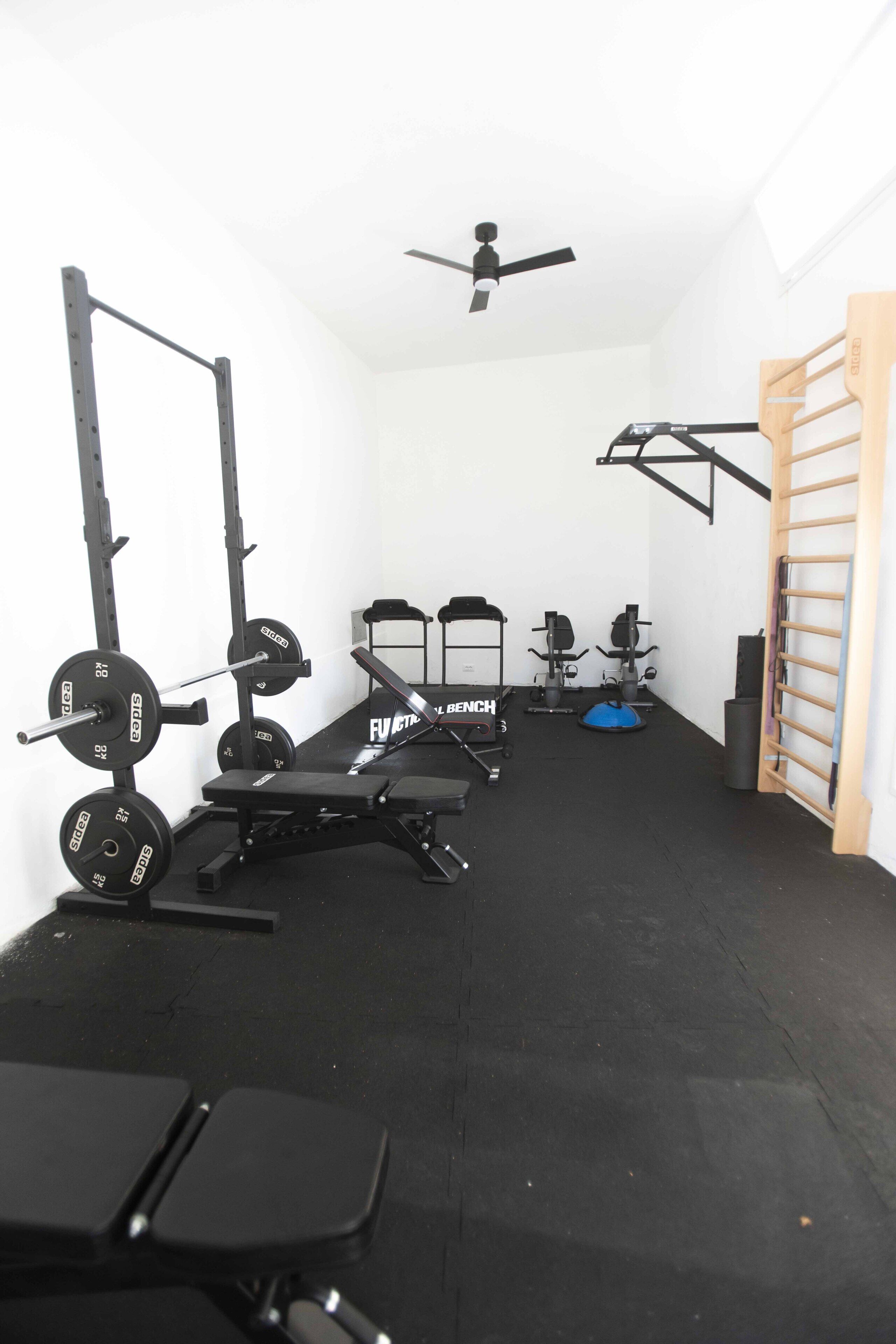 A gym with weightlifting equipment, a bench, and a ceiling fan.