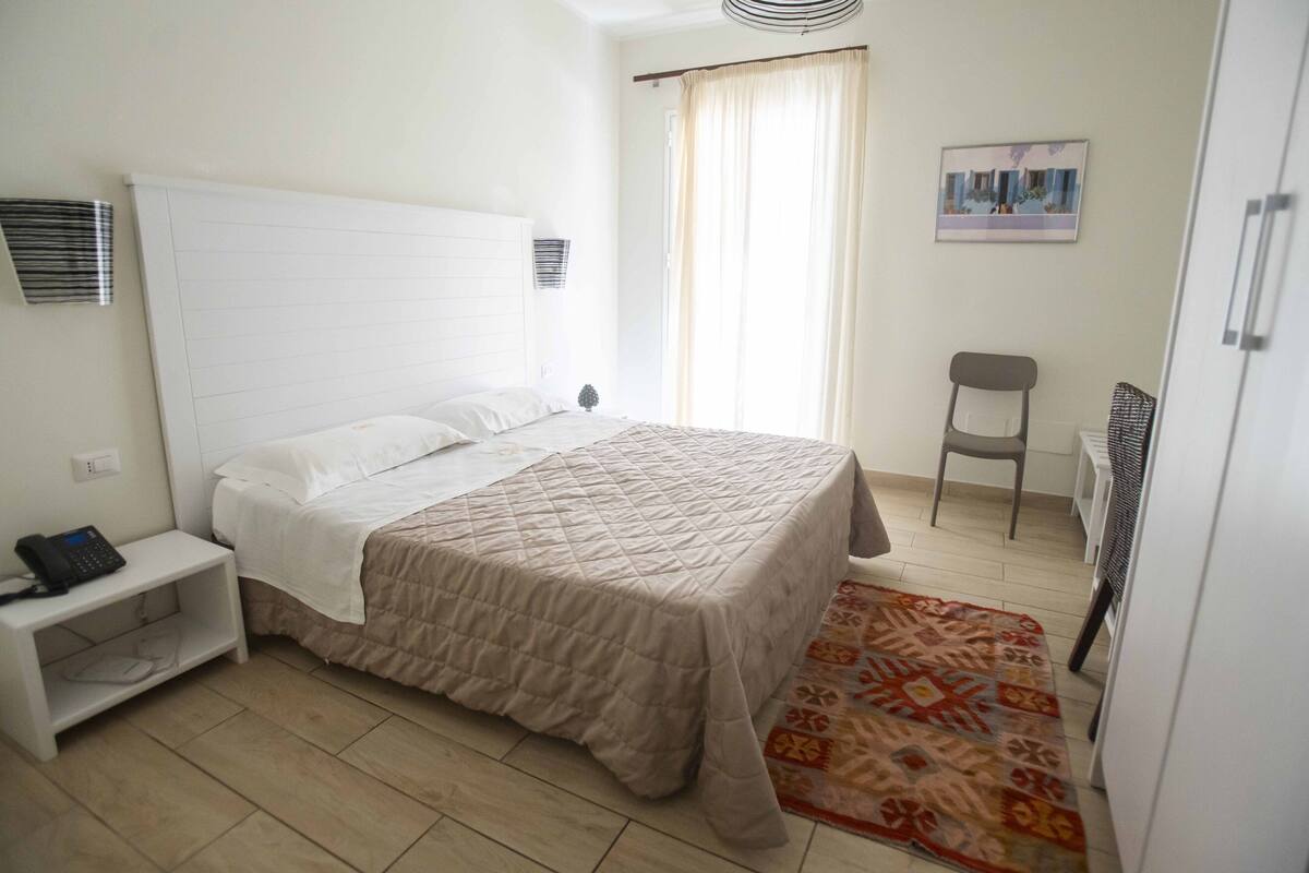 A bedroom with a bed, a nightstand, a chair, and a radiator.