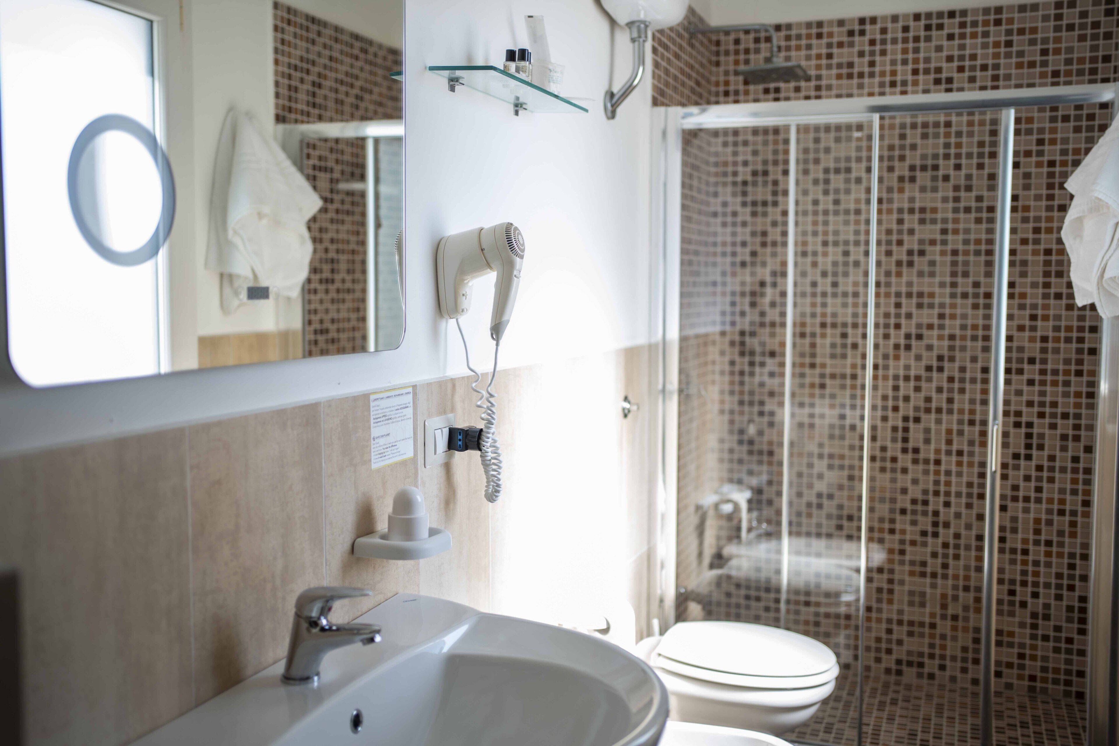 A bathroom with a sink, mirror, hairdryer, and shower area.