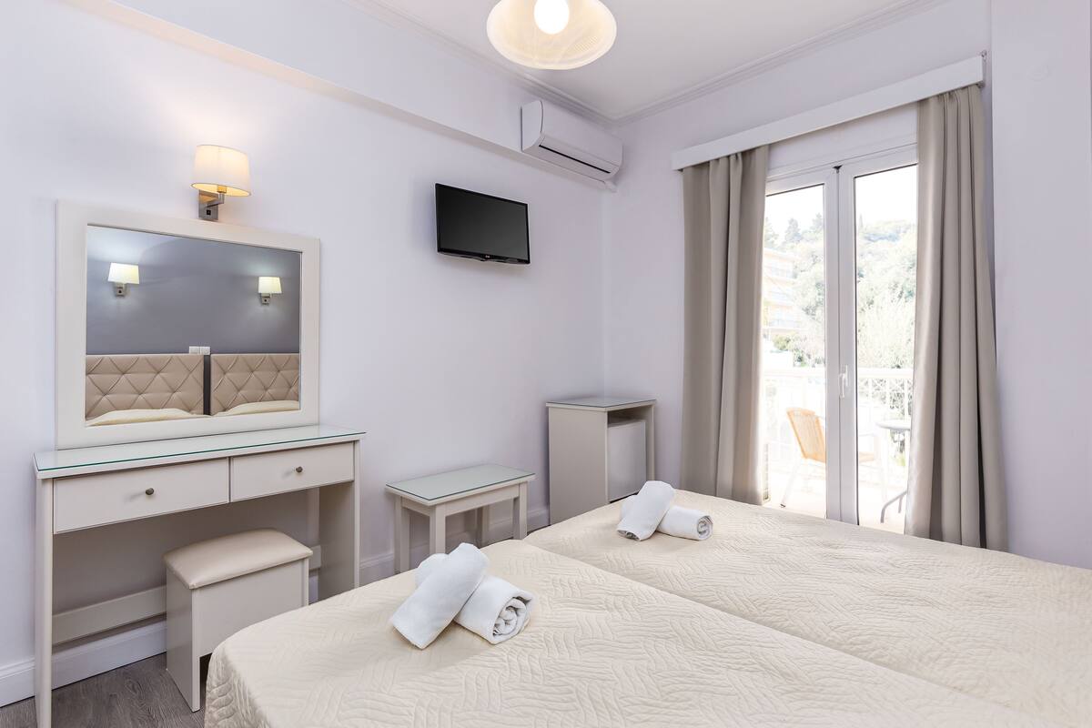 Une chambre d’hôtel avec deux lits, une télévision, un miroir, un bureau et une fenêtre avec des rideaux.