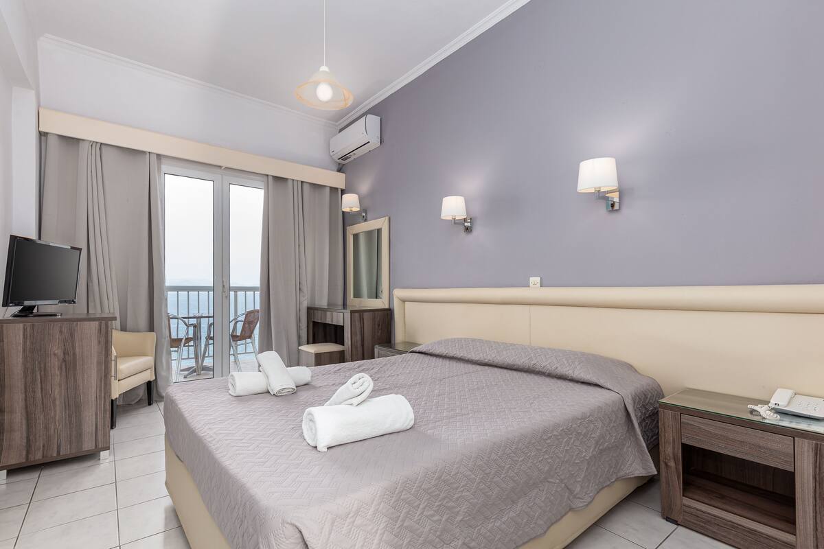 Une chambre d’hôtel comprenant un lit, un bureau, une télévision, un balcon avec vue et deux lampes fixées au mur.