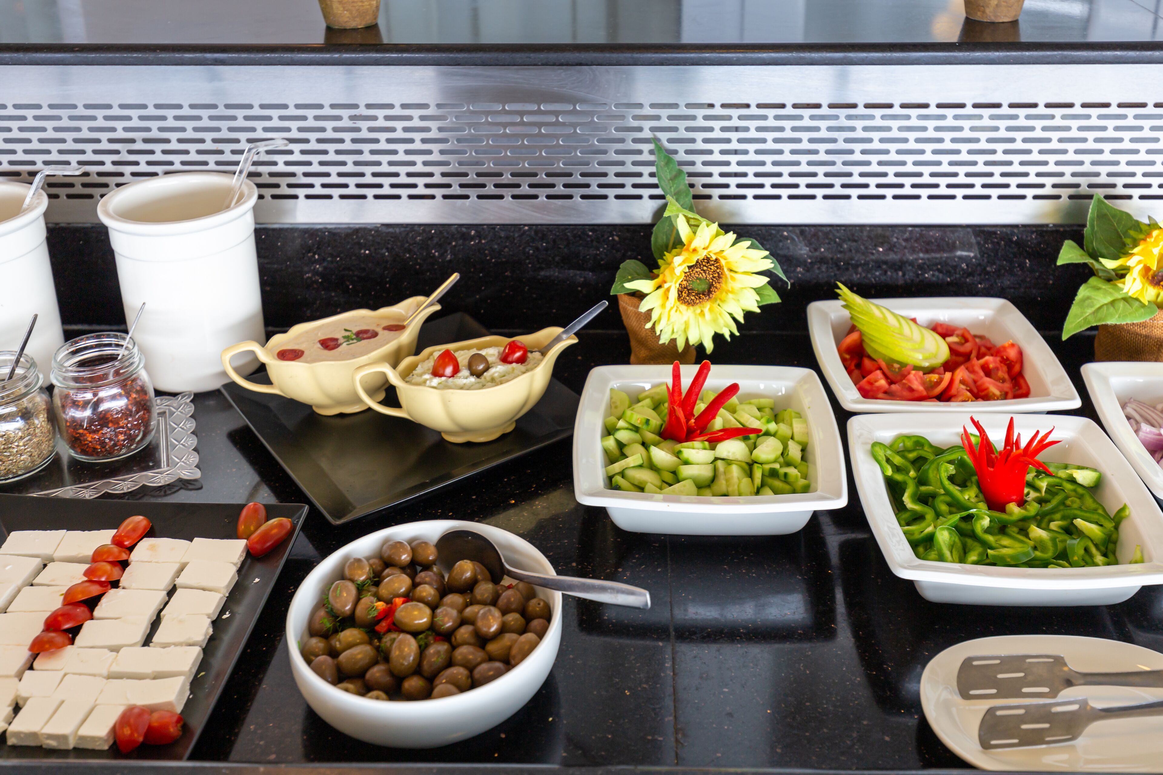 Une table de buffet proposant divers aliments, notamment du fromage, des olives, des concombres, des tomates et des poivrons.