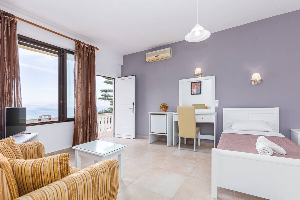 Une chambre d’hôtel avec un lit, un bureau, une chaise, un canapé, une télévision et une vue sur la mer.