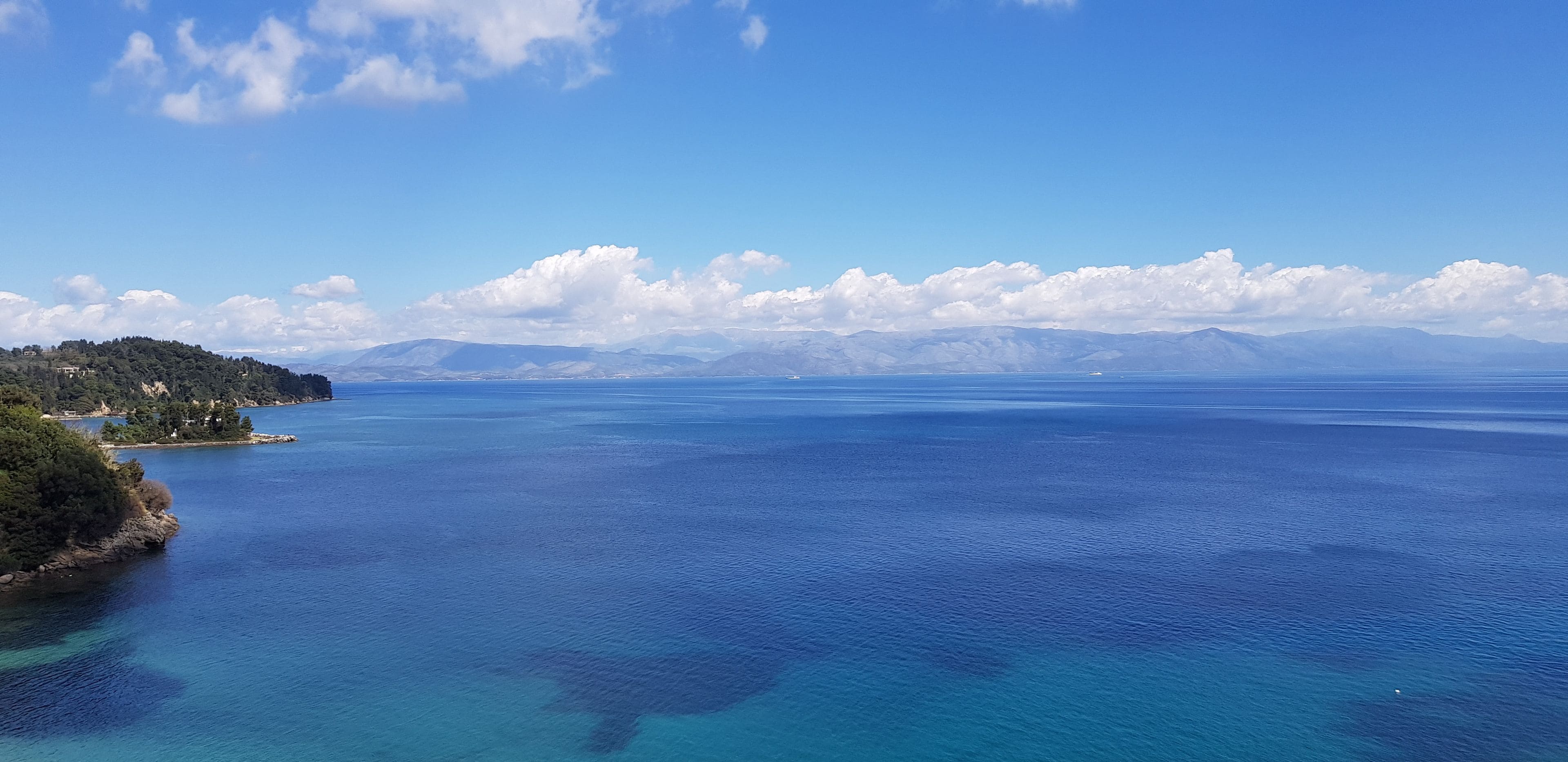 A coastal landscape with a clear sky, calm sea, and distant mountains.