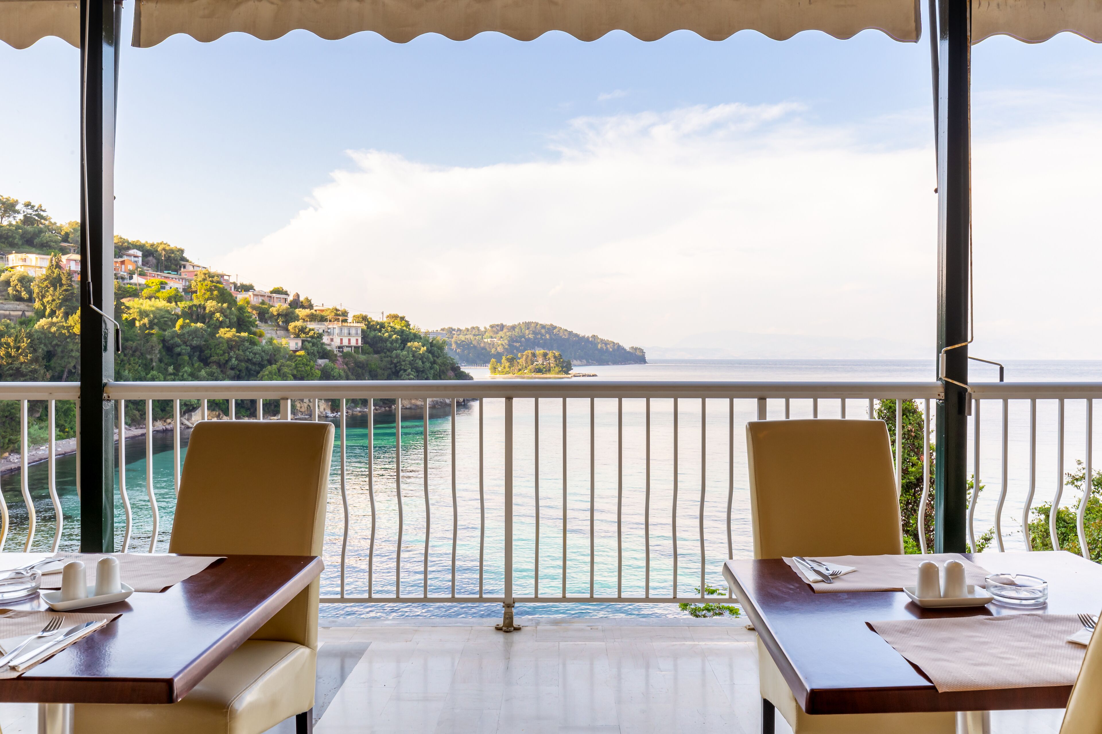 A dining area with a view of a coastal landscape, including a body of water and a hillside with buildings.