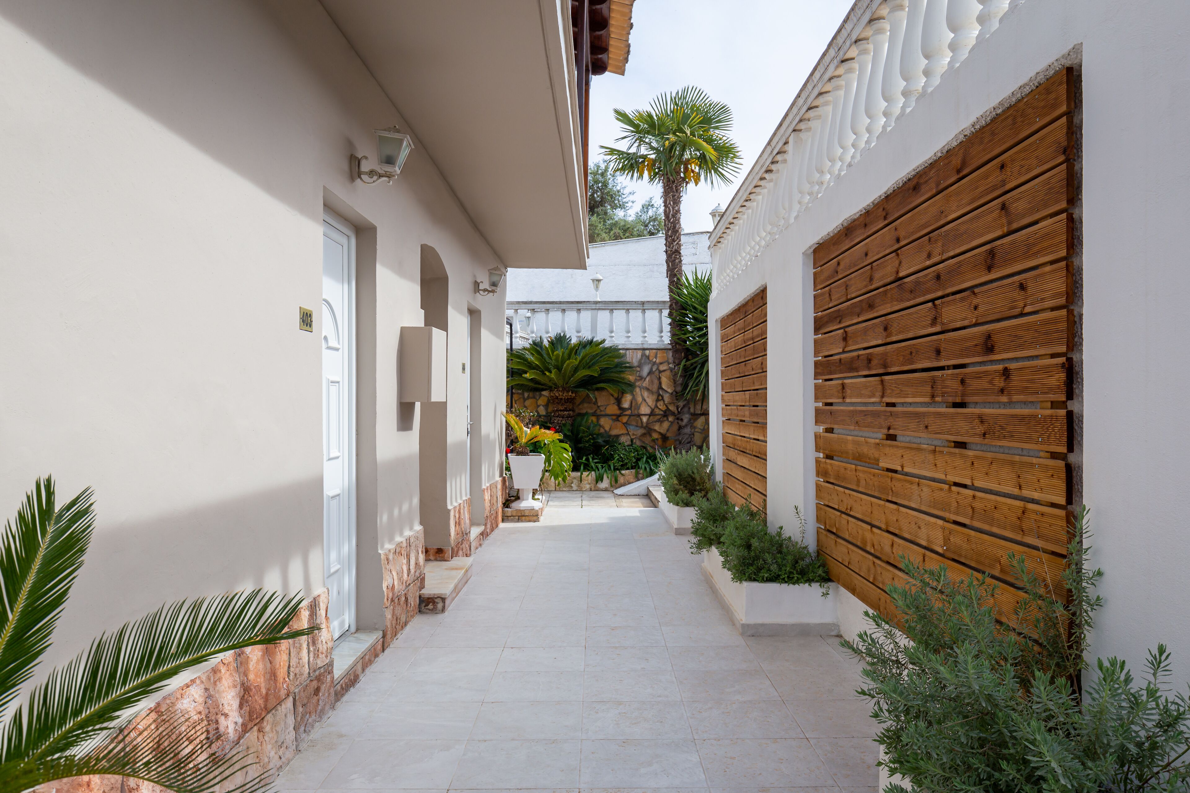 A narrow, paved pathway flanked by white walls and wooden paneling, leading to a building entrance.