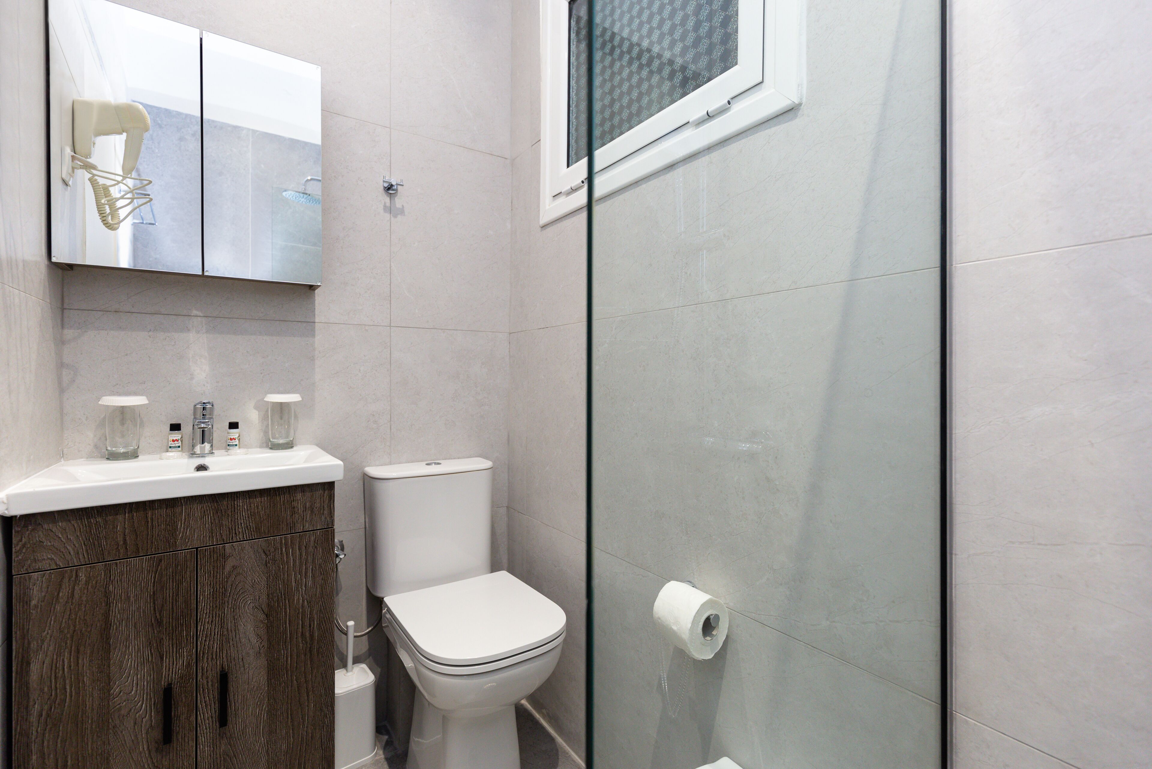 A modern bathroom with a toilet, a sink with two faucets, and a shower area with a glass door.