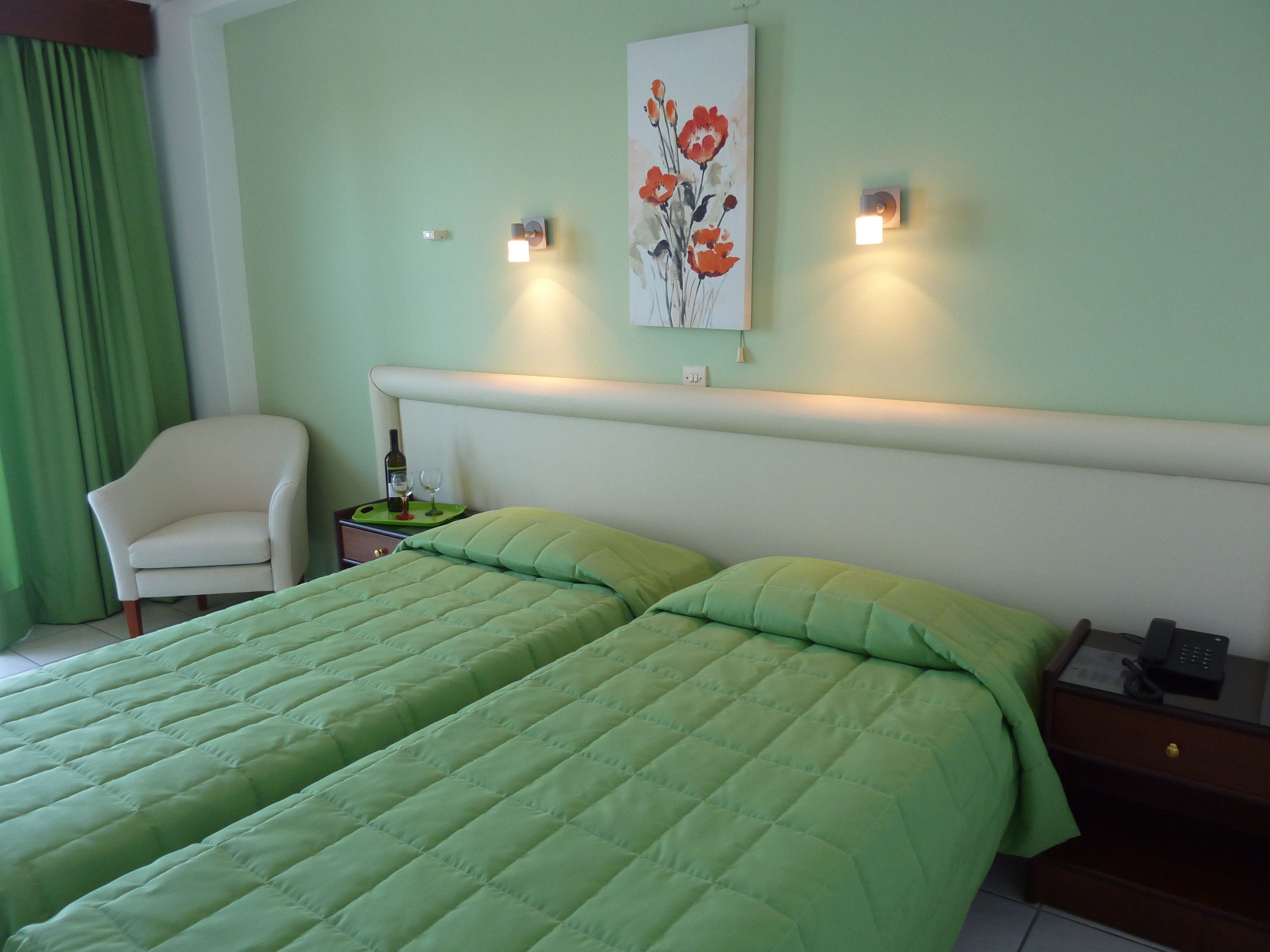 A hotel room with two beds, a chair, a nightstand with a phone, and a painting on the wall.