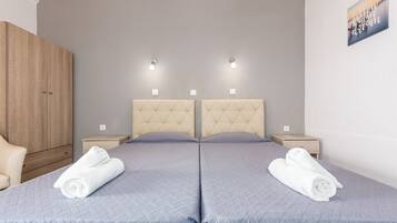 Un dormitorio doble con dos camas, un armario de madera, mesitas de noche y una lámpara fijada a la pared.