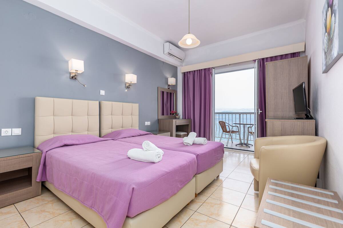 Une chambre d’hôtel avec deux lits, un bureau, une chaise et un balcon avec vue.