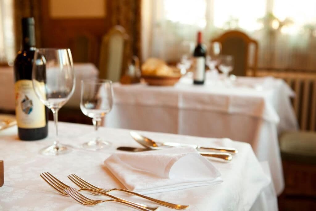 Mesa de comedor decorada con cubiertos dorados, copas de vino y una botella de vino, evocando una experiencia culinaria elegante.