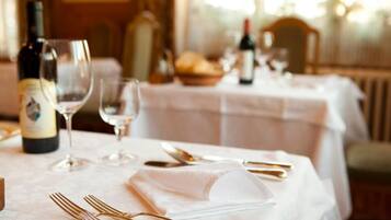 Mesa de comedor decorada con cubiertos dorados, copas de vino y una botella de vino, evocando una experiencia culinaria elegante.