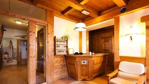 A wooden reception desk with a chair, a hanging light fixture, and a door with a wooden frame. - Hotel Bellaria (Cortina d'Ampezzo)
