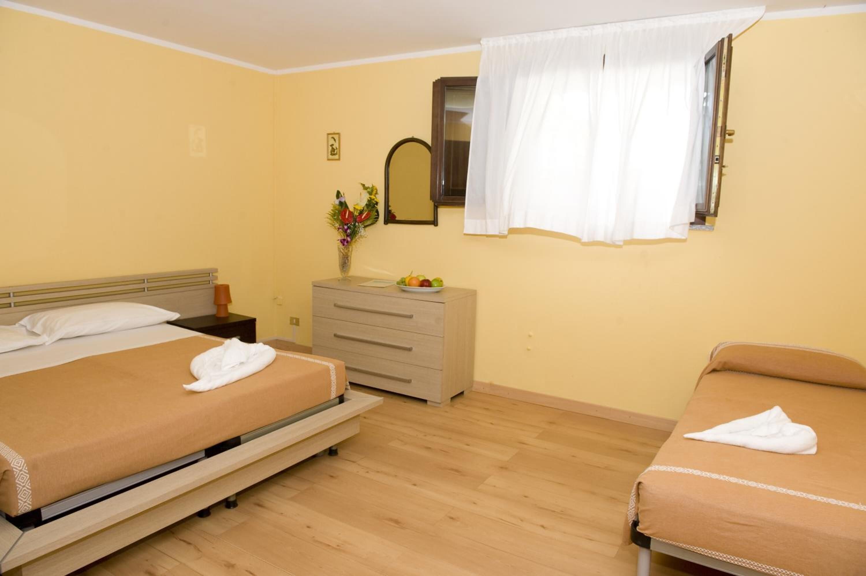 A hotel room with two beds, a dresser, a mirror, and a window with white curtains.
