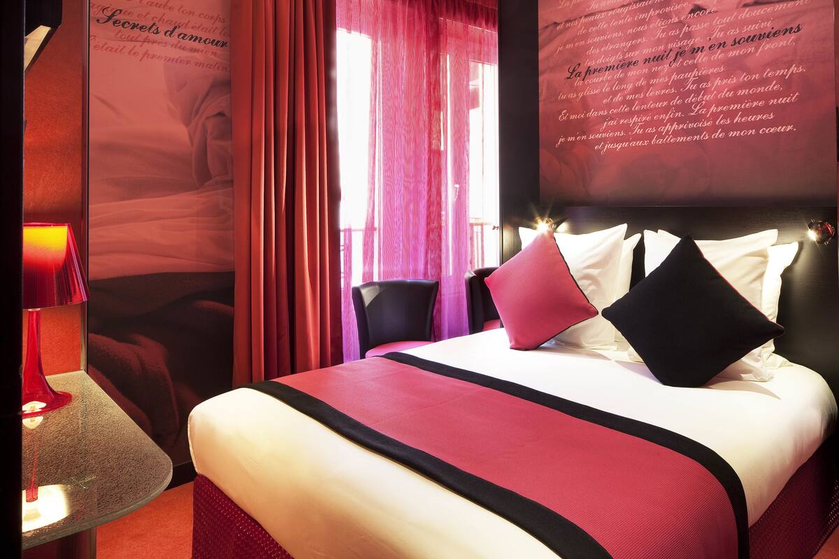 A hotel room with a bed, a nightstand, a lamp, and curtains.