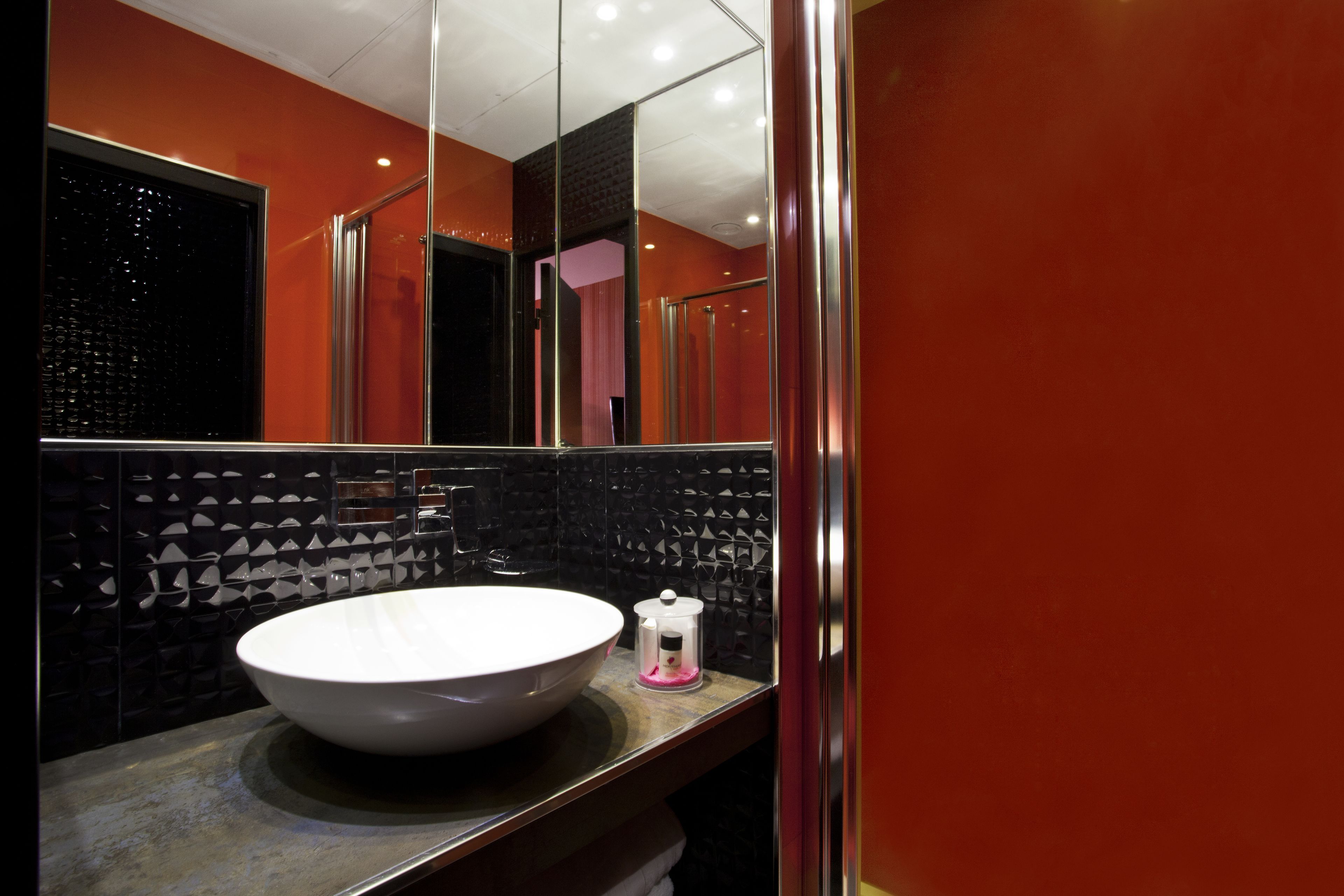 A modern bathroom with a large oval sink, a mirror, and a black textured wall.