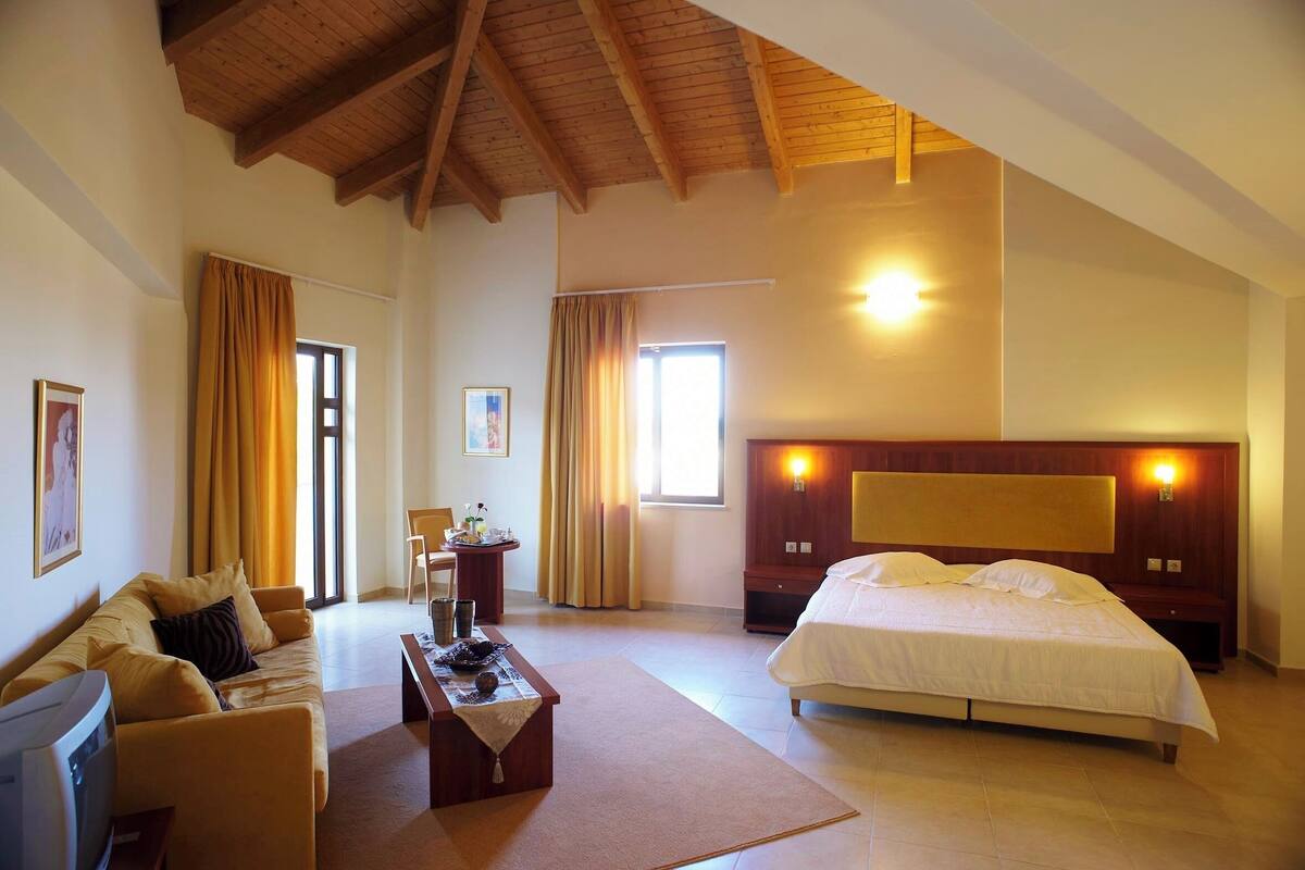 Um quarto espaçoso com uma cama grande, cabeceira de madeira e teto com vigas aparentes.