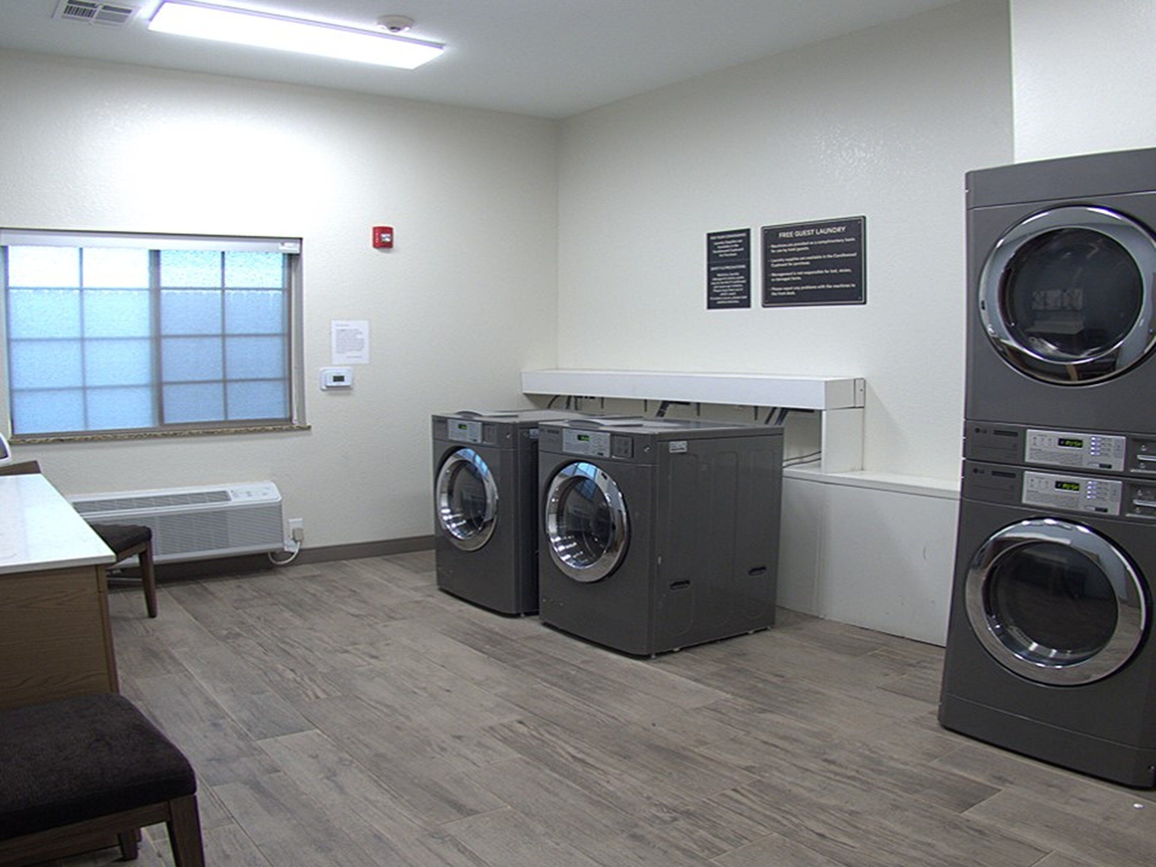 A laundry facility with two front-loading washers, a dryer, a bench, and a window providing natural light.