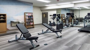 Un gimnasio con equipo de ejercicio, una banca y una estantería.