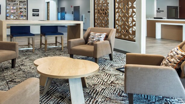 A modern lobby with a reception desk, seating area with chairs and a round table, decorative screens, and a visible kitchenette area. - Candlewood Suites Avondale - New Orleans by IHG (Westwego)