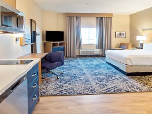 Habitación de hotel con cama, escritorio con silla, televisor, ventana con cortinas y alfombra.