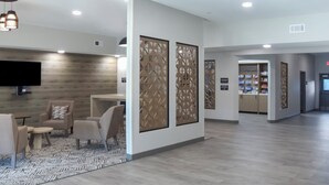 Un vestíbulo amplio con diseño moderno, que presenta una pared de madera, un área de descanso con sillas y una mesita, y una recepción.