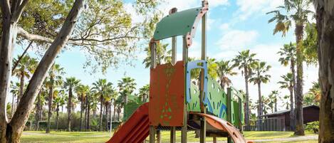 Une aire de jeux avec des toboggans et des structures d’escalade, entourée d’arbres et sous un ciel dégagé.