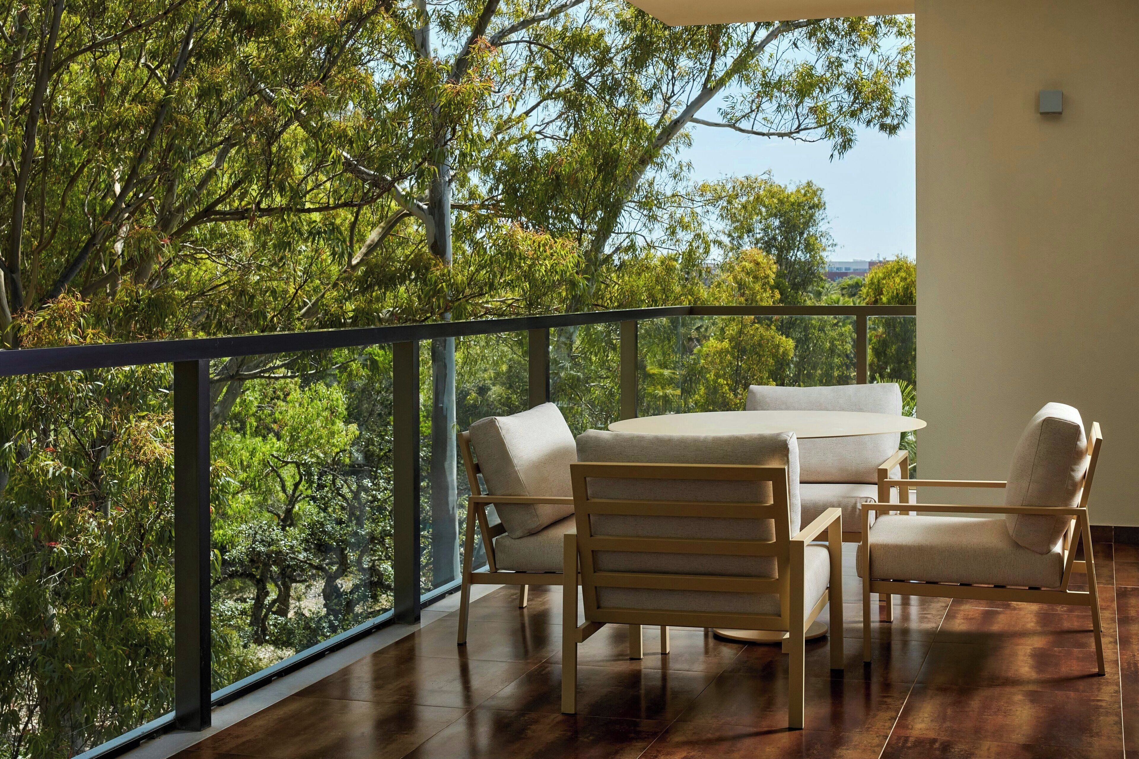 Un balcon avec une table et des chaises en bois, donnant sur un paysage verdoyant et luxuriant.