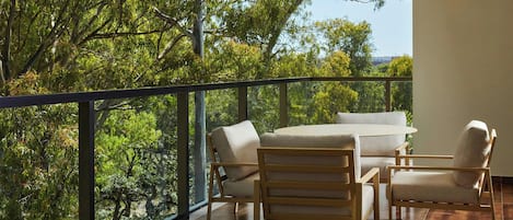 A balcony with a wooden table and chairs, overlooking a lush green landscape.