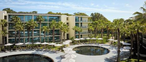 A resort with a pool area, lounge chairs, umbrellas, and palm trees.