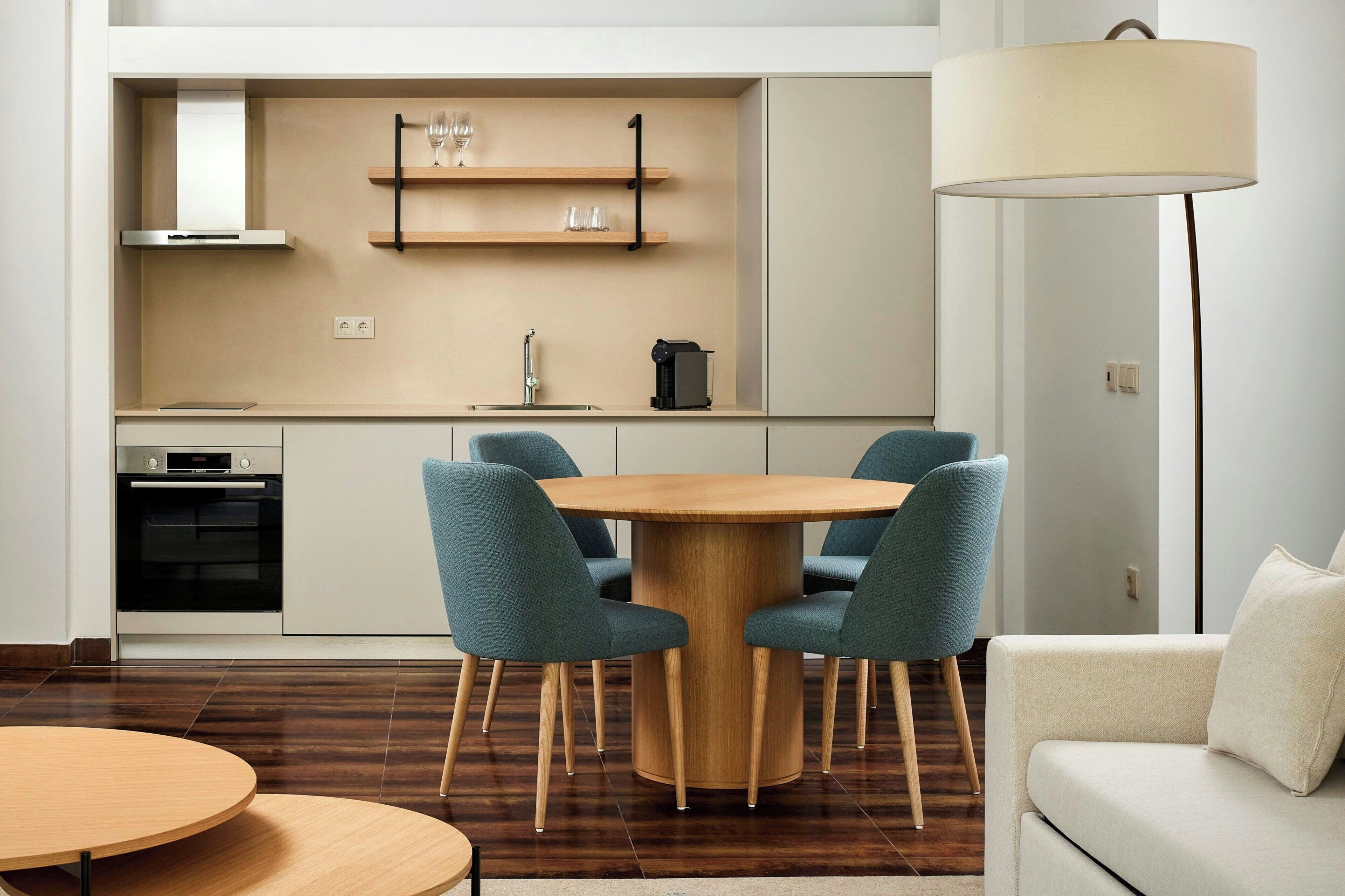 A modern kitchen with a round wooden table and four chairs, a built-in oven, and a coffee machine.