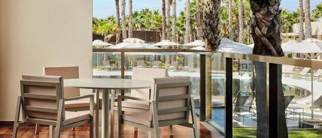 Un balcon avec une table et des chaises, donnant sur un espace piscine agrémenté de palmiers et de parasols.