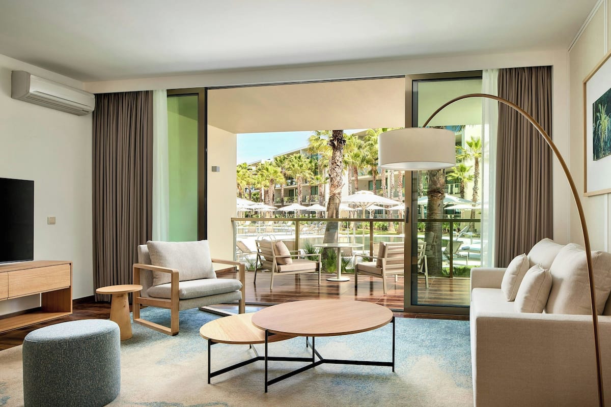 Ein modernes Hotelzimmer mit großem Balkon, einem Flachbildfernseher, einer Couch, einem Couchtisch und einem Essbereich mit Sitzgelegenheiten im Freien.