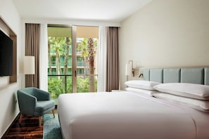 A hotel room with a large bed, a chair, a TV, and a view of palm trees through the window.