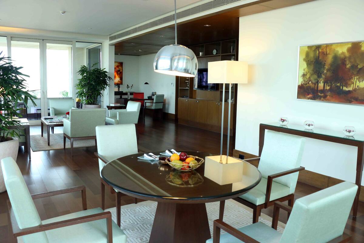 Uma sala de jantar moderna com mesa de vidro, cadeiras brancas, uma cesta de frutas e uma luminária pendente.
