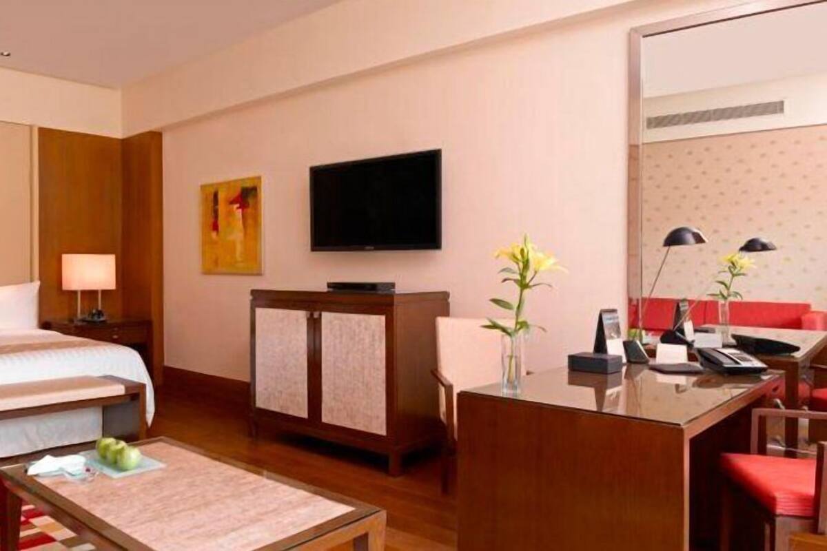 Quarto de hotel com cama, mesas de cabeceira, escrivaninha com cadeira, televisão e espelho.