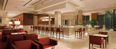 Un amplio vestíbulo de hotel con una zona de bar central, diversas opciones de asientos que incluyen cabinas y mesas, y una planta grande en la esquina.