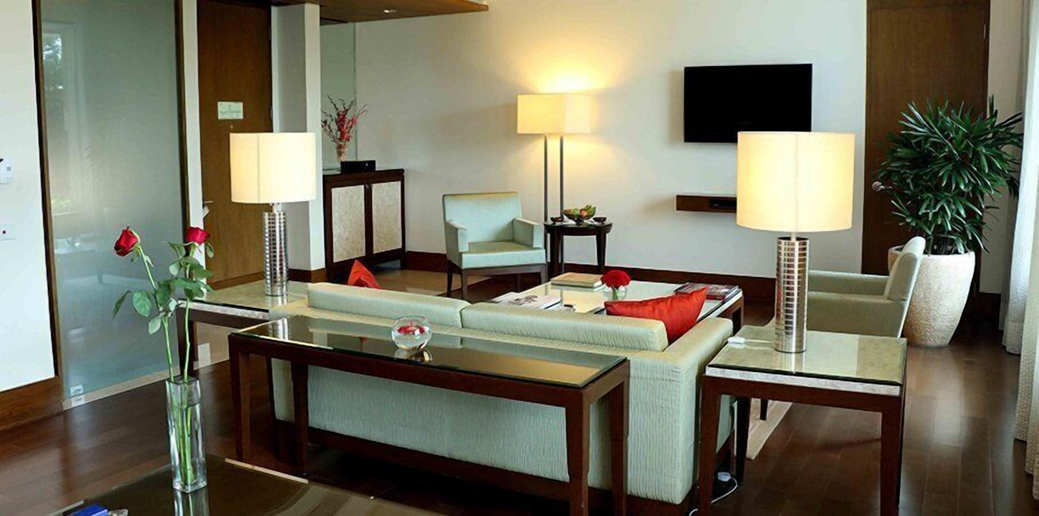Una habitación de hotel moderna con sofá, sillones, una mesa de centro y un televisor instalado en la pared.