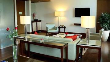 Una habitación de hotel moderna con sofá, sillones, una mesa de centro y un televisor instalado en la pared.