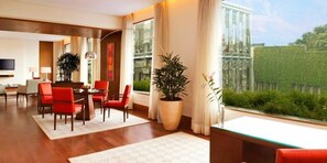 A modern hotel room with a dining area, large windows, and a view of the greenery outside. - The Oberoi Gurgaon (Gurugram)