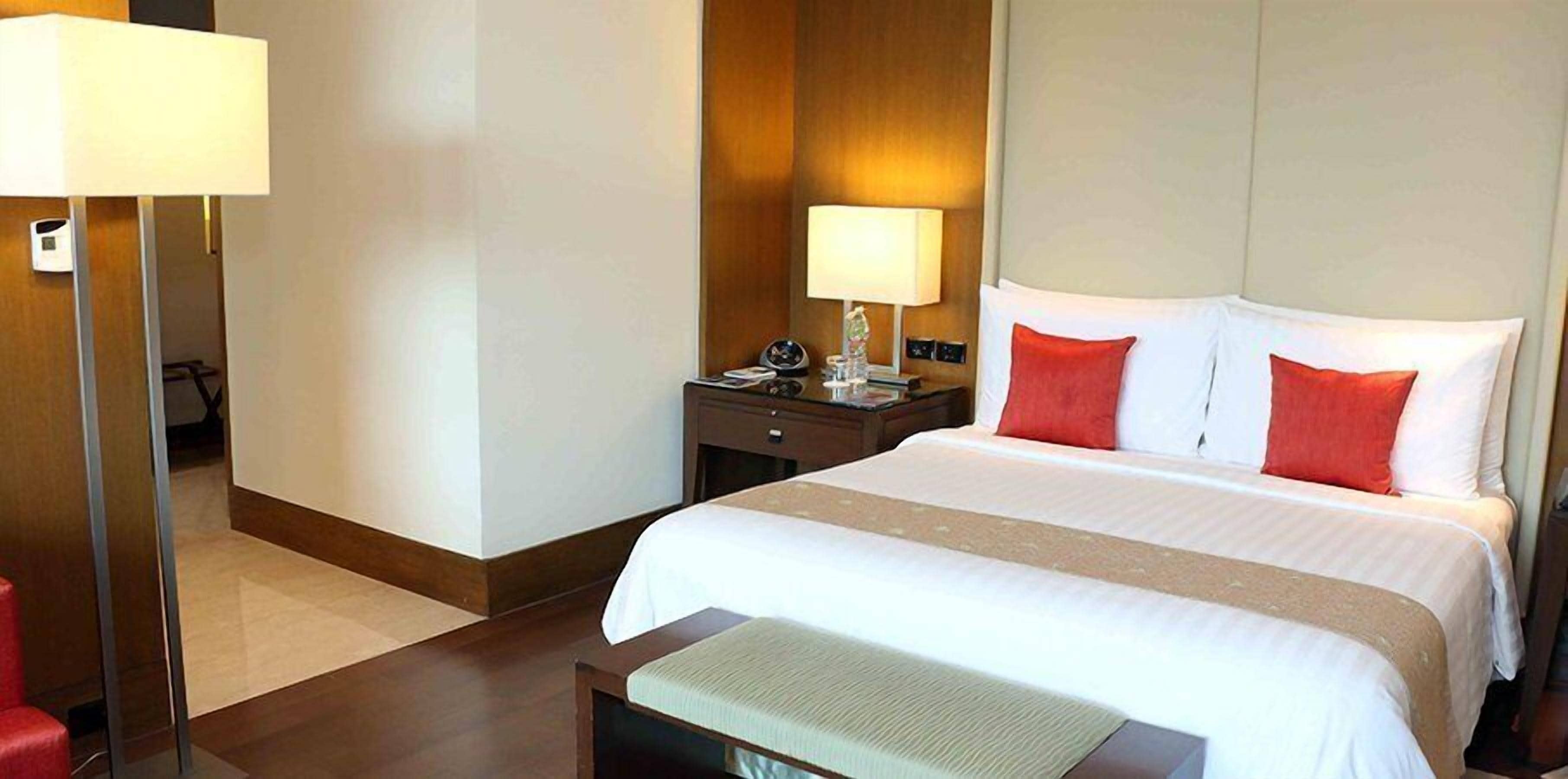 A hotel room with a large bed, a bedside table with a lamp, a red chair, and a wooden floor.