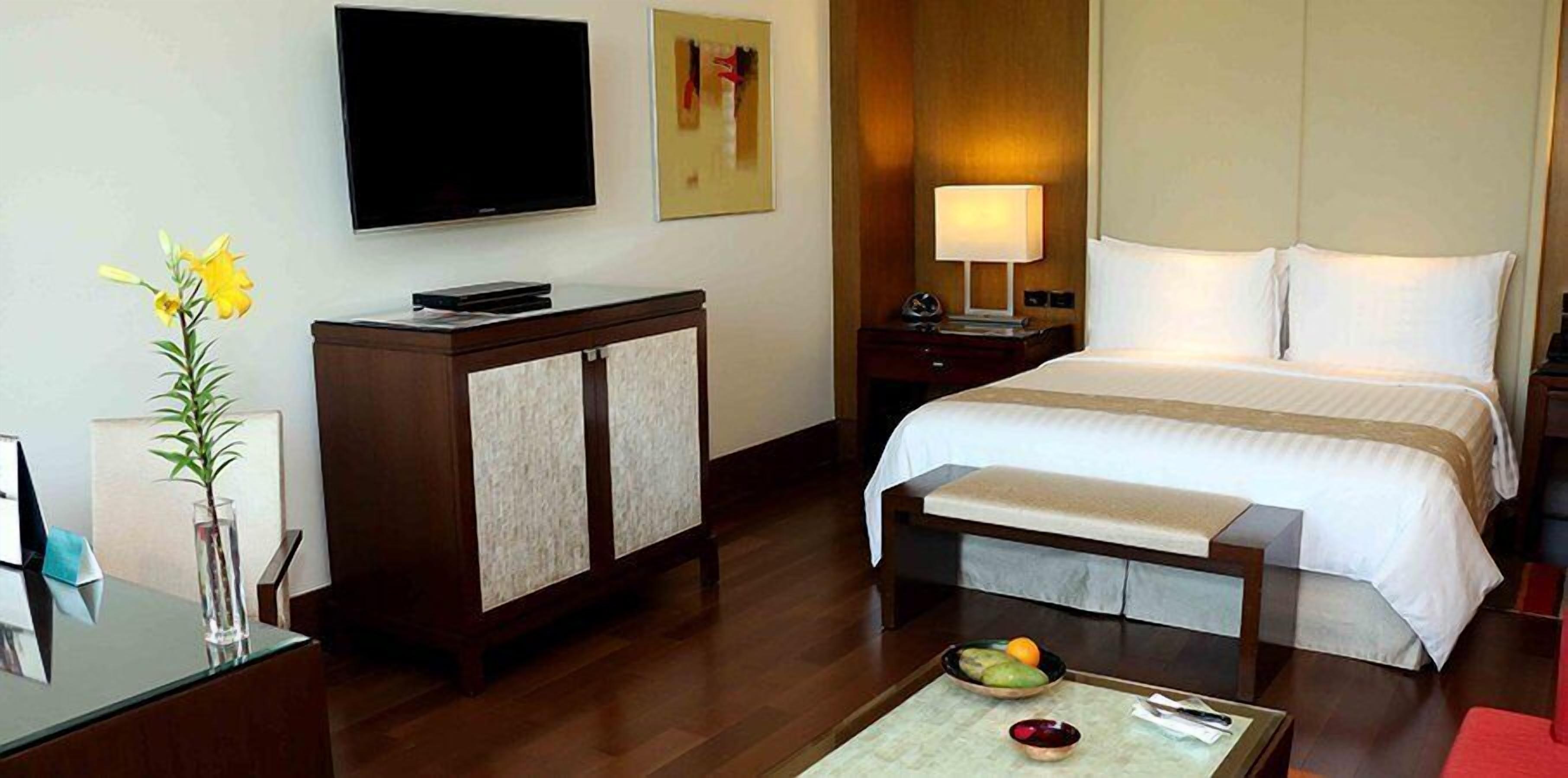 Une chambre d’hôtel comprenant un lit, un bureau, une télévision, une table de chevet, une lampe et un vase avec des fleurs.
