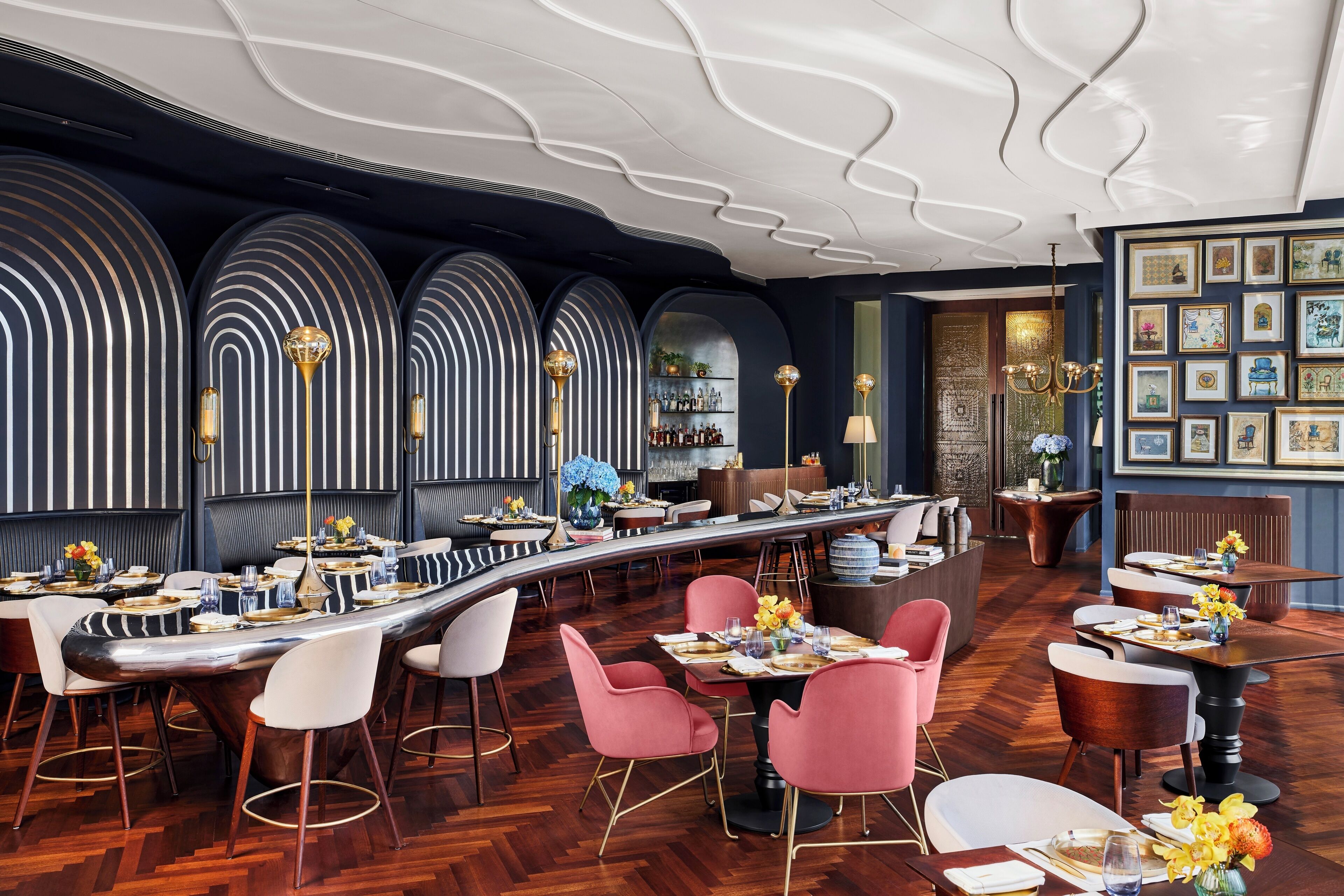 A modern restaurant with a long bar, multiple seating areas, and a decorative ceiling.